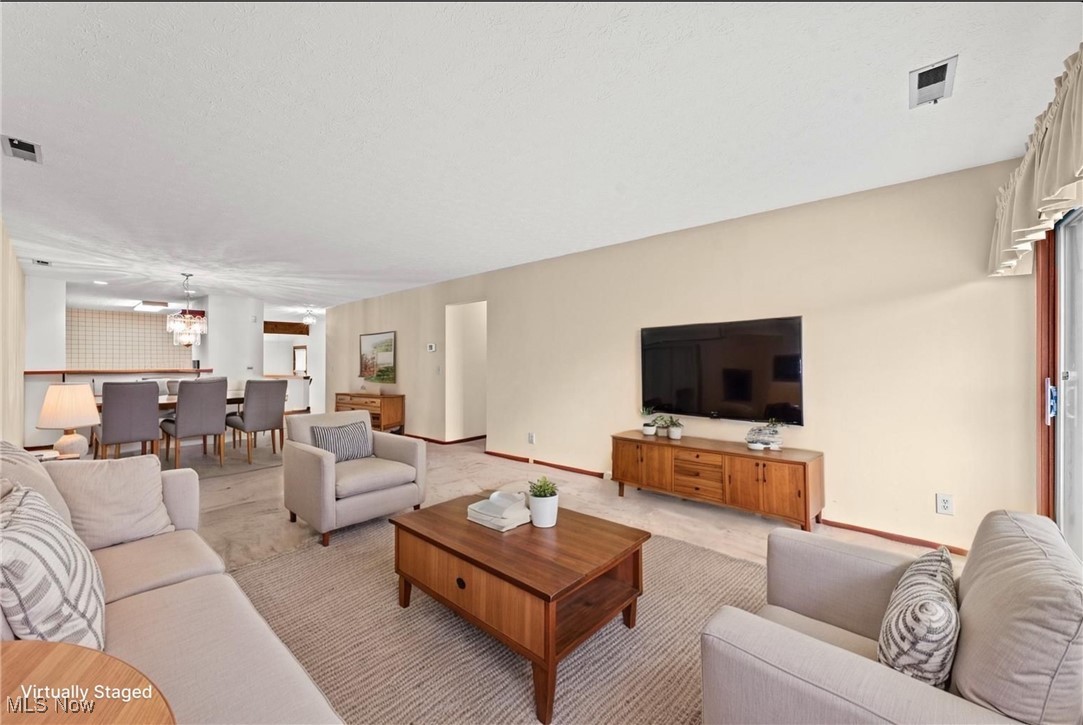 Virtually staged living room with neutral seating, wood furniture, and an adjoining dining area.