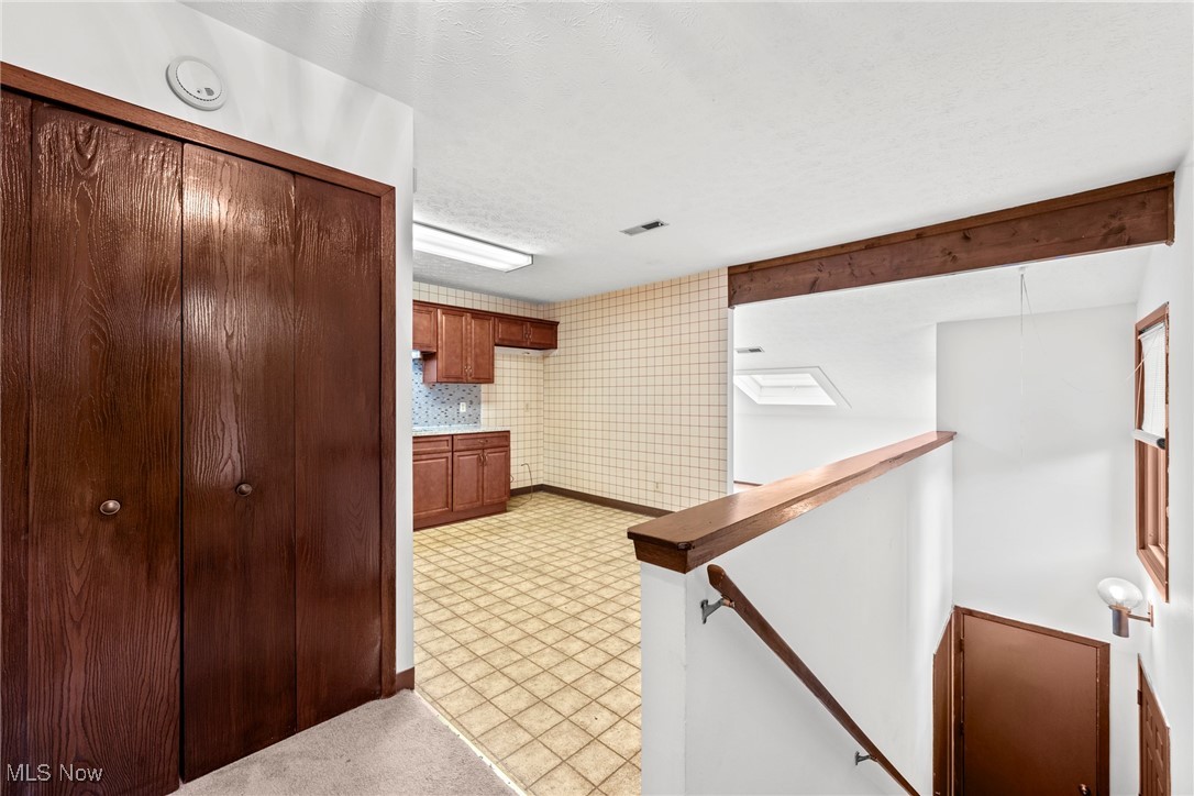 Upper landing overlooking a tiled kitchen, with dark wood closet doors and a wood-capped stair railing.