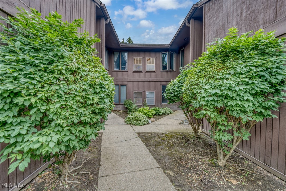 Two-story brown-sided residence viewed from a shrub-lined courtyard with a paved walkway.