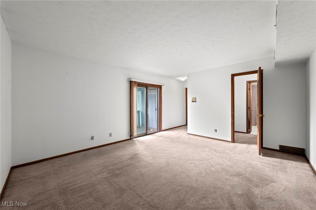 Empty carpeted room with a sliding glass door and dark wood trim.