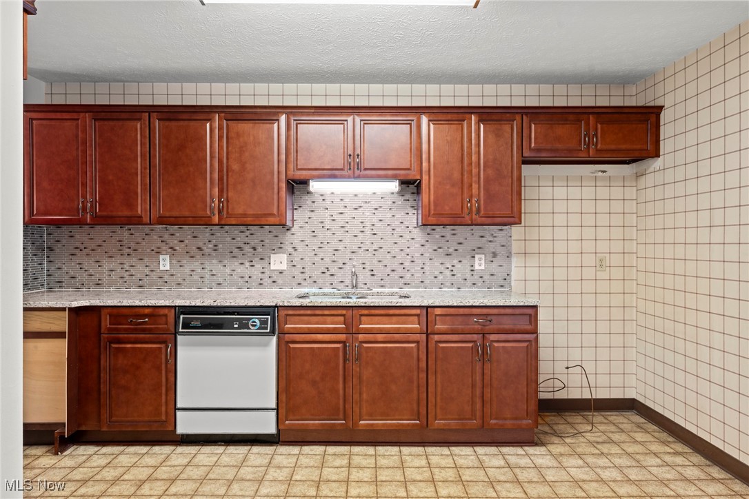 Kitchen with reddish-brown cabinets, gray mosaic backsplash, and built-in dishwasher.