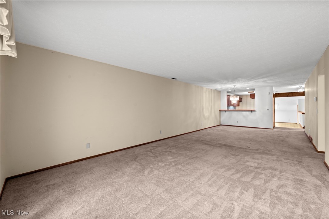 Long vacant carpeted basement room with a pass-through counter and adjoining kitchenette.
