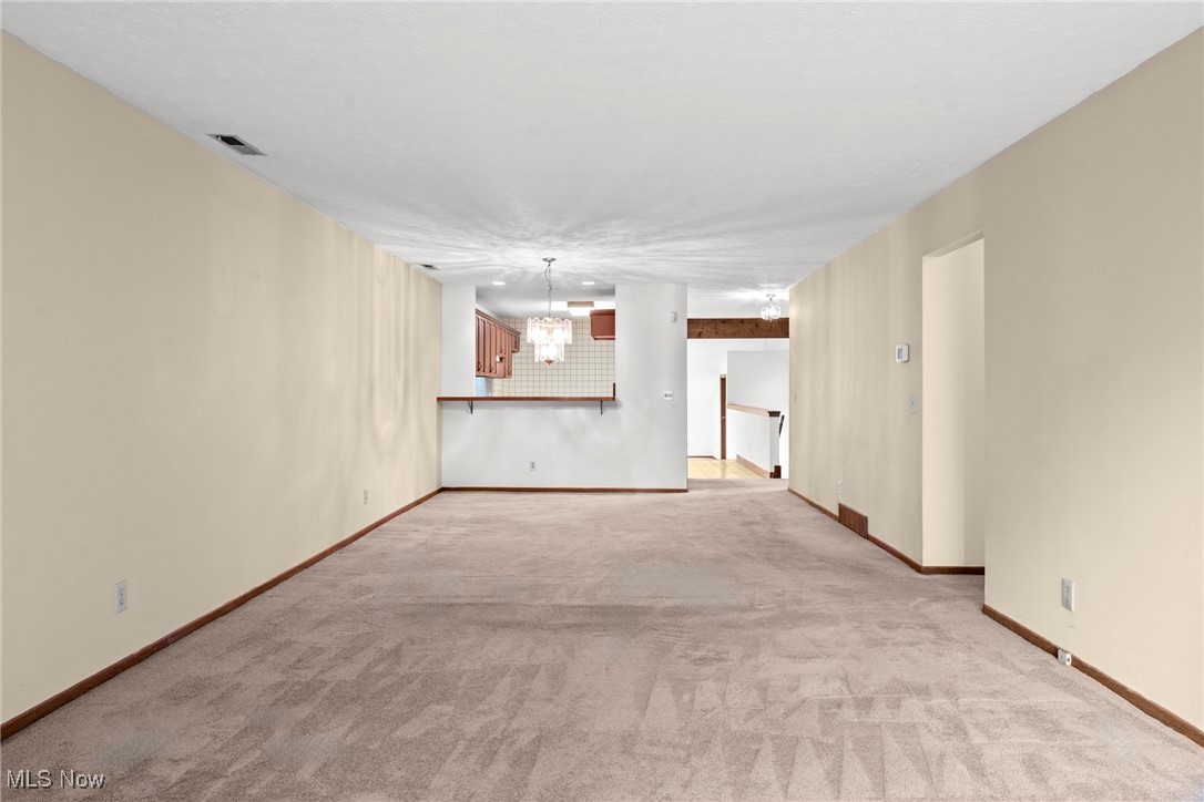 Empty carpeted living room with a pass-through opening to the kitchen.