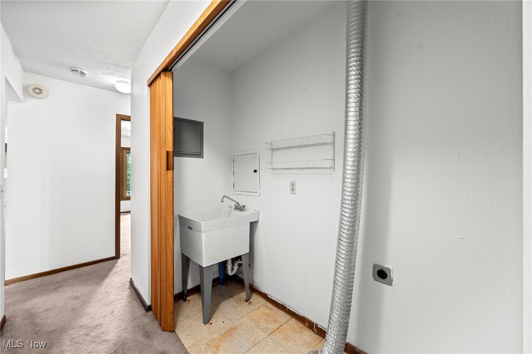 Utility room with a deep sink, exposed metal duct, and wire shelving beside a carpeted hallway.