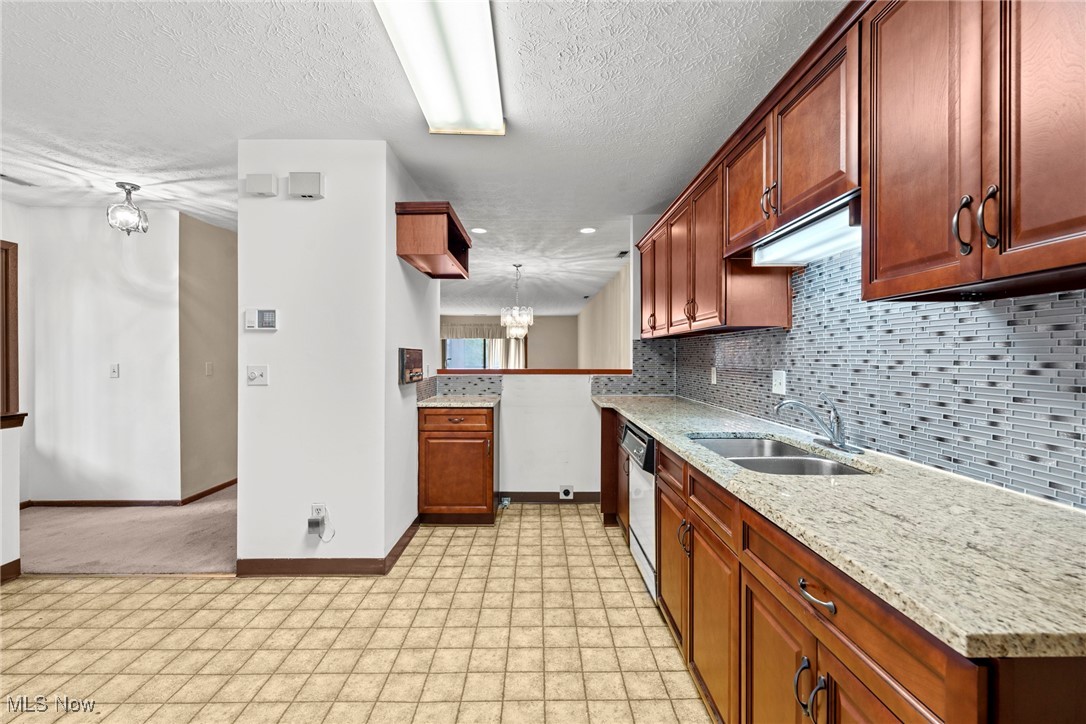 Kitchen with reddish-brown cabinets, granite counters, double sink, and gray mosaic tile backsplash.