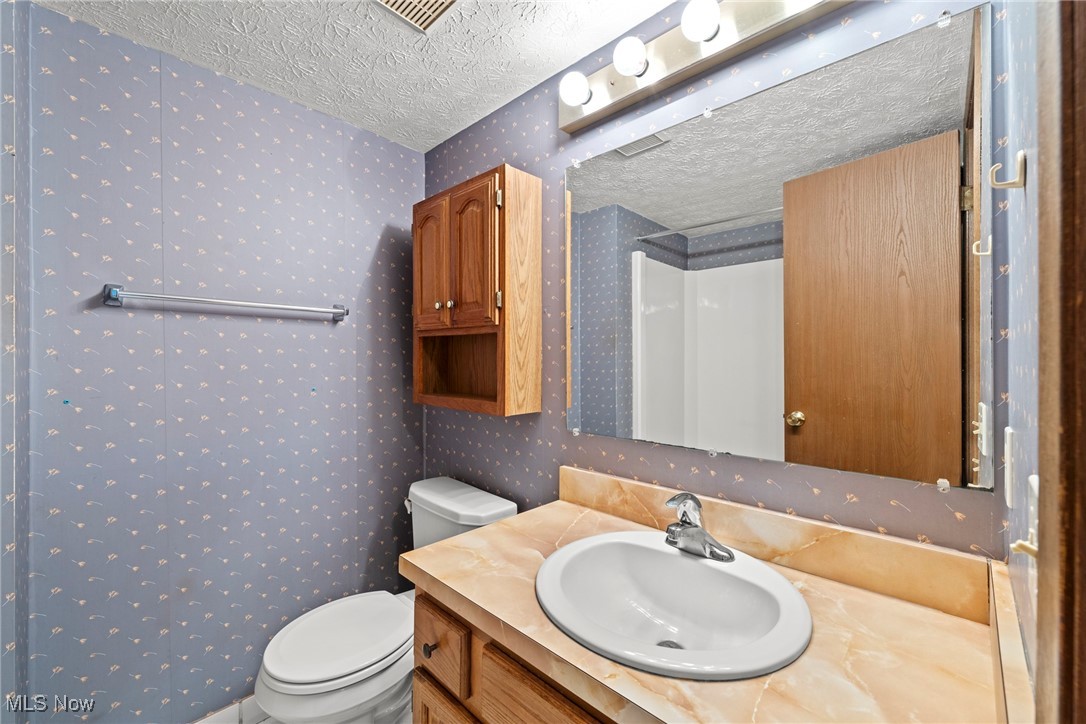 Bathroom with a peach vanity, wood cabinetry, large mirror, and blue patterned wallpaper.