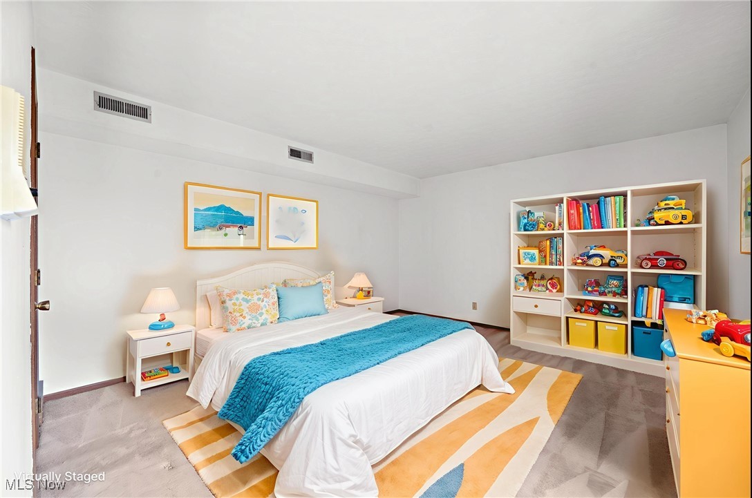 Virtually staged bedroom with a white bed, turquoise throw, colorful toy shelves, and striped rug.