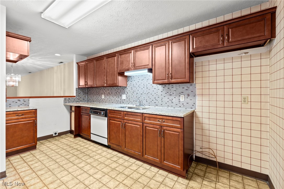 Kitchen with reddish-brown cabinets, gray mosaic backsplash, and stainless-steel dishwasher.