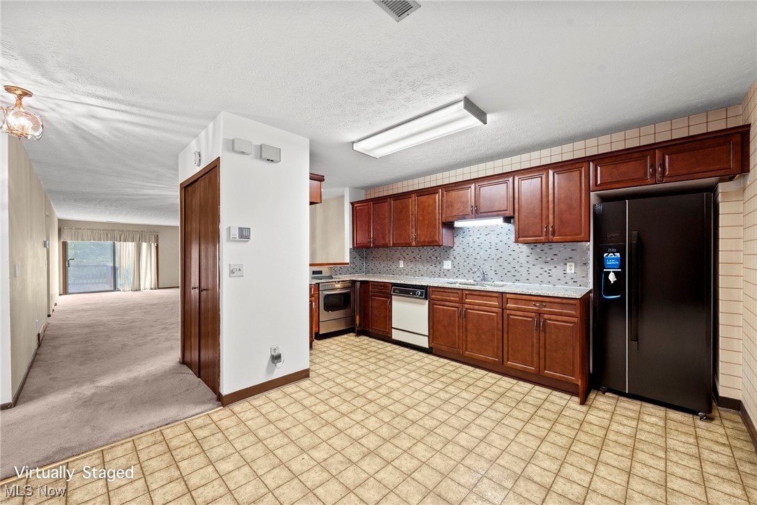Kitchen with reddish-brown cabinets and tiled floors, opening onto an empty carpeted living area.