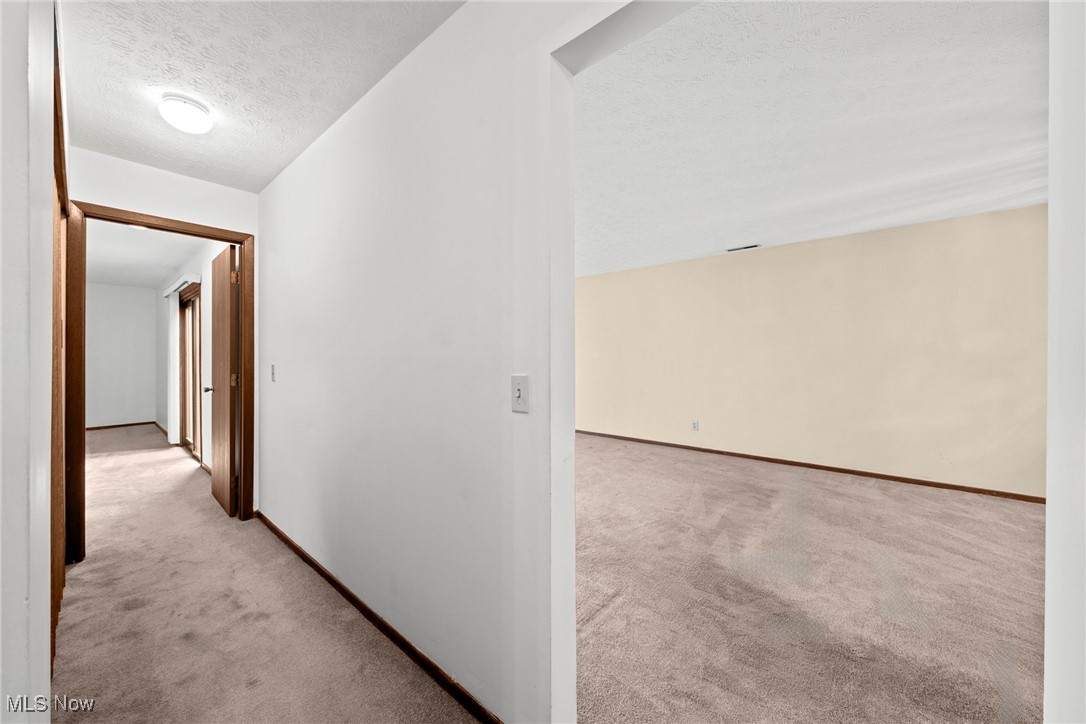 Carpeted hallway opening into an empty room with beige walls and dark wood trim.