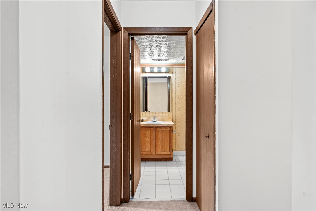Bathroom with a wood vanity and tiled floor, viewed through open wooden doors.
