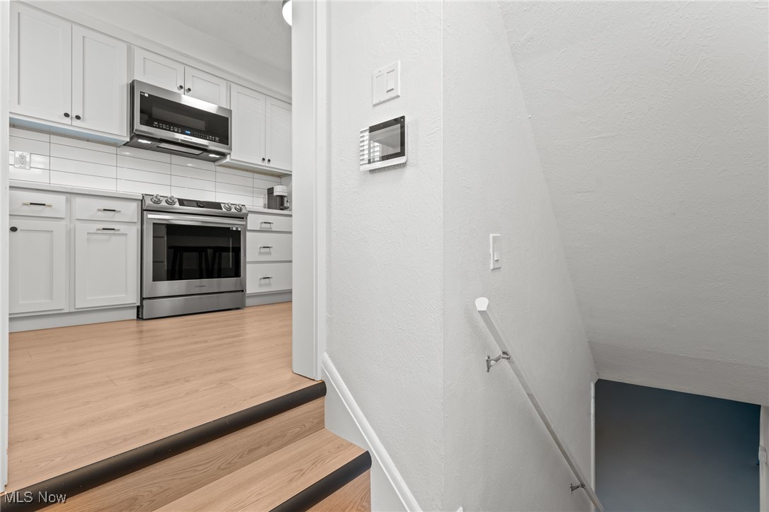 White kitchen with stainless steel appliances, seen beside stairs descending to a lower level.