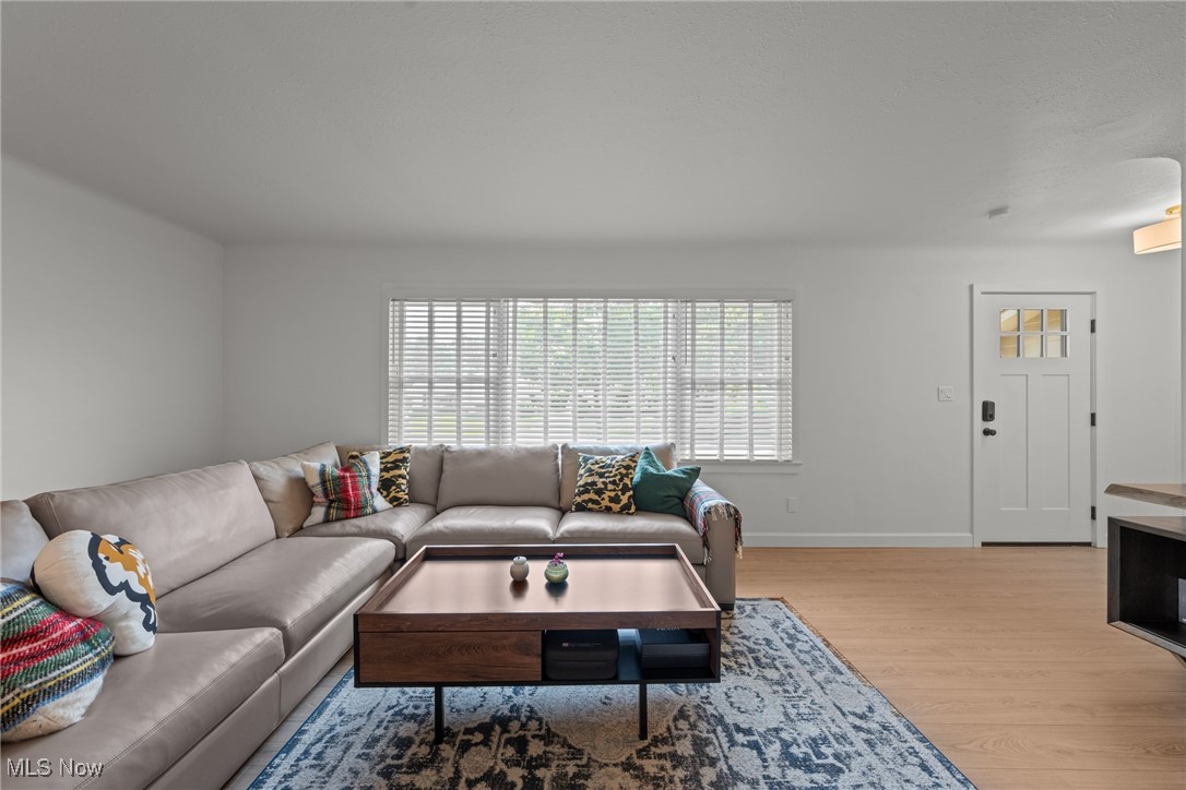 Living room with a sectional sofa, wood coffee table, patterned rug, and wide window with blinds.