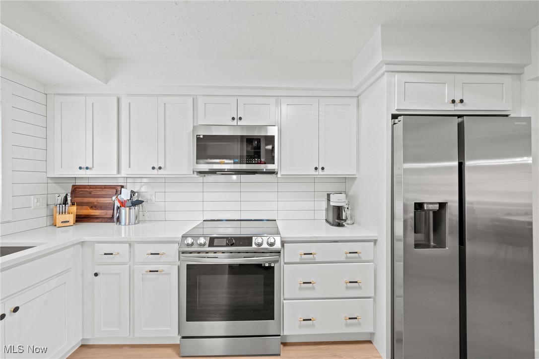 White kitchen with shaker cabinets, tile backsplash, and stainless steel appliances.