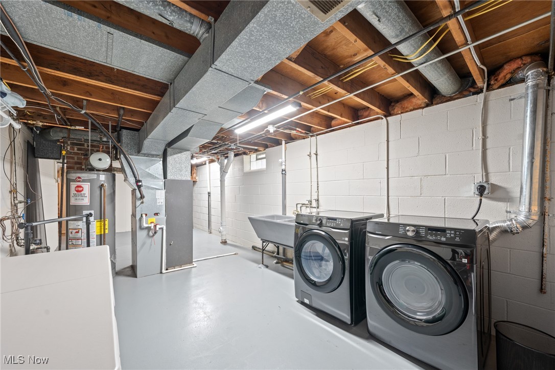 Basement laundry room with front-loading washer and dryer, utility sink, and exposed ceiling joists.