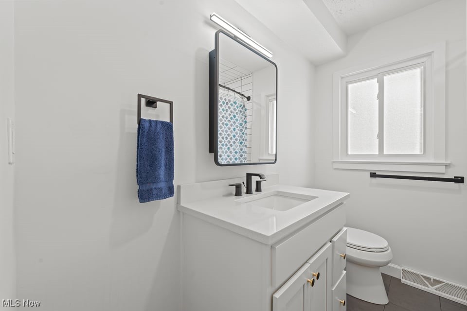 Bathroom with a white vanity, black faucet, toilet, and window.