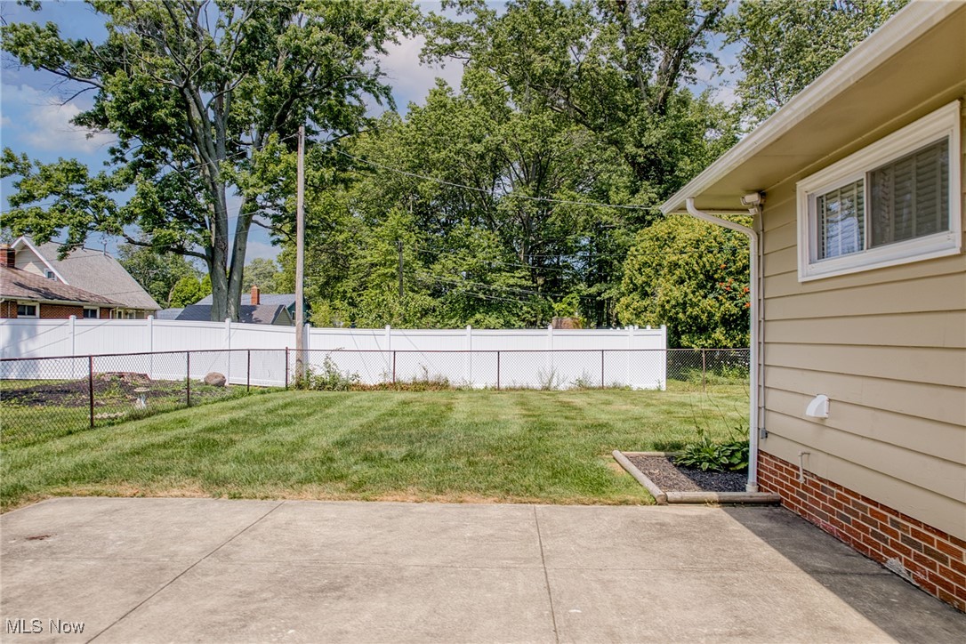 Backyard with a concrete patio, broad lawn, and white and chain-link fences.