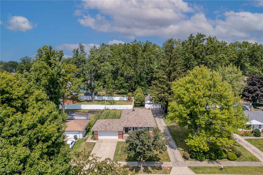Aerial view of a single-story ranch home with a broad driveway and mature trees.