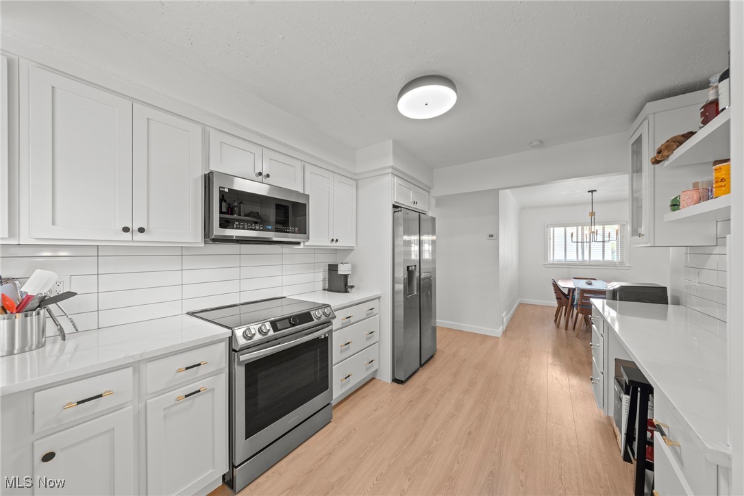 Kitchen with white shaker cabinets, stainless steel appliances, and a dining table by the window.