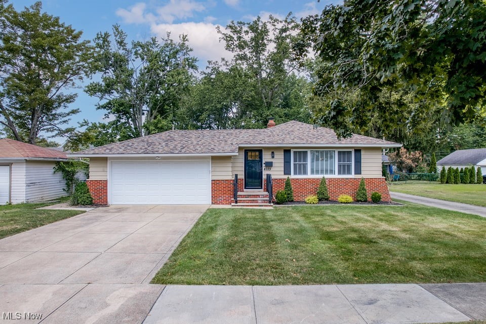 Single-story brick-and-siding home with an attached garage, wide driveway, and trimmed lawn.