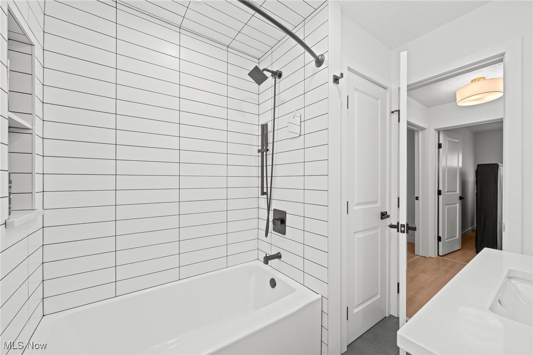 Bathroom with a white tiled tub and shower, rainfall showerhead, and white vanity.