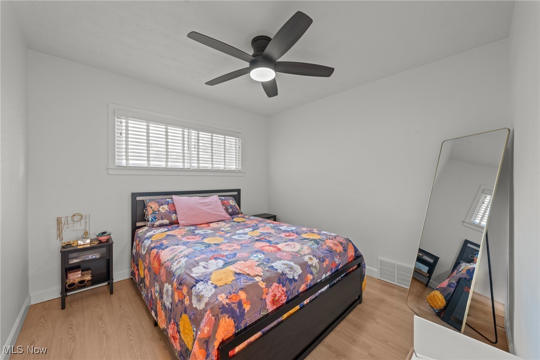 Bedroom with colorful floral bedding, a dark wood bed frame, ceiling fan, and leaning full-length mirror.