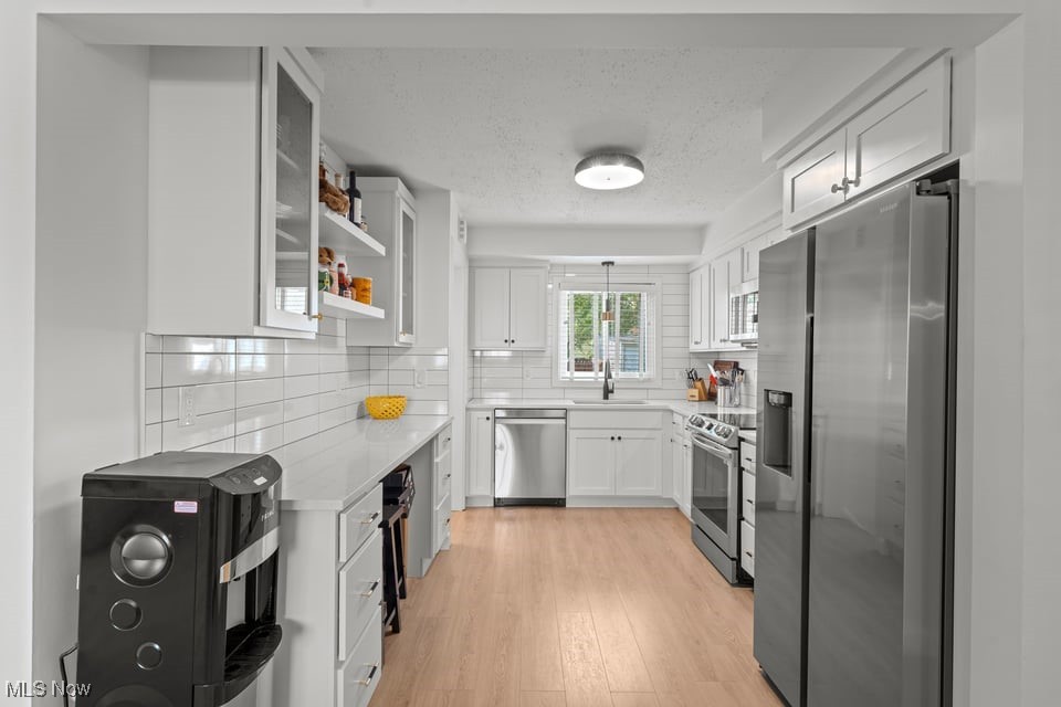 Bright white kitchen with subway tile backsplash, stainless steel appliances, and light wood flooring.