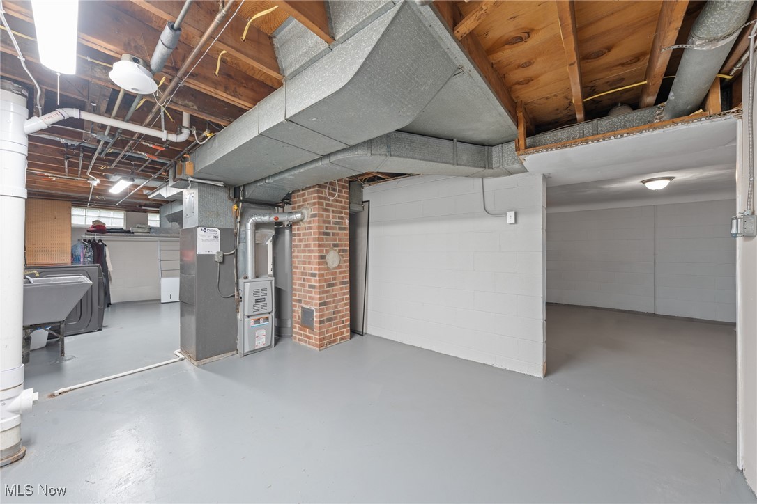Unfinished basement with exposed ceiling joists, HVAC ducts, mechanical equipment, and a laundry area.