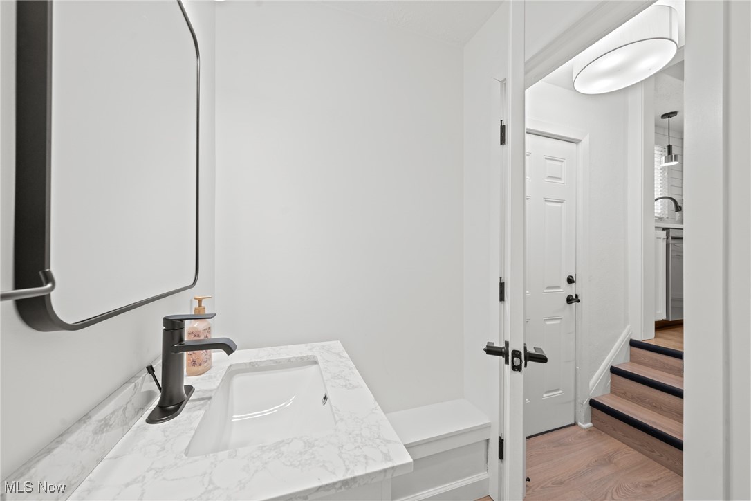 Bathroom vanity with marble-pattern countertop and black faucet beside a doorway to wood steps.
