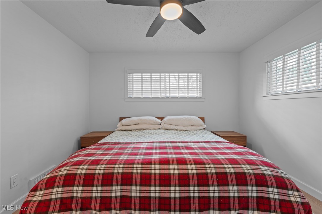 Bedroom with a red plaid comforter, wooden bedside tables, and windows with white blinds.