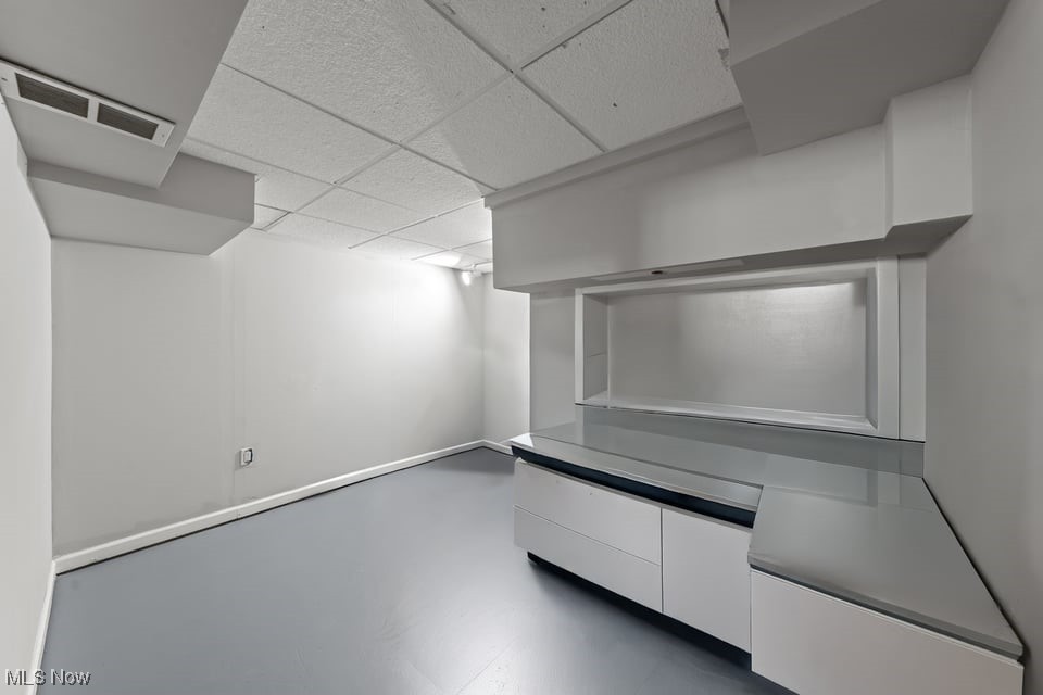 Empty basement room with gray flooring and a built-in counter and cabinets.
