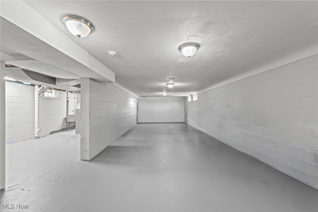 Empty basement with painted block walls, concrete floor, and exposed utility pipes.