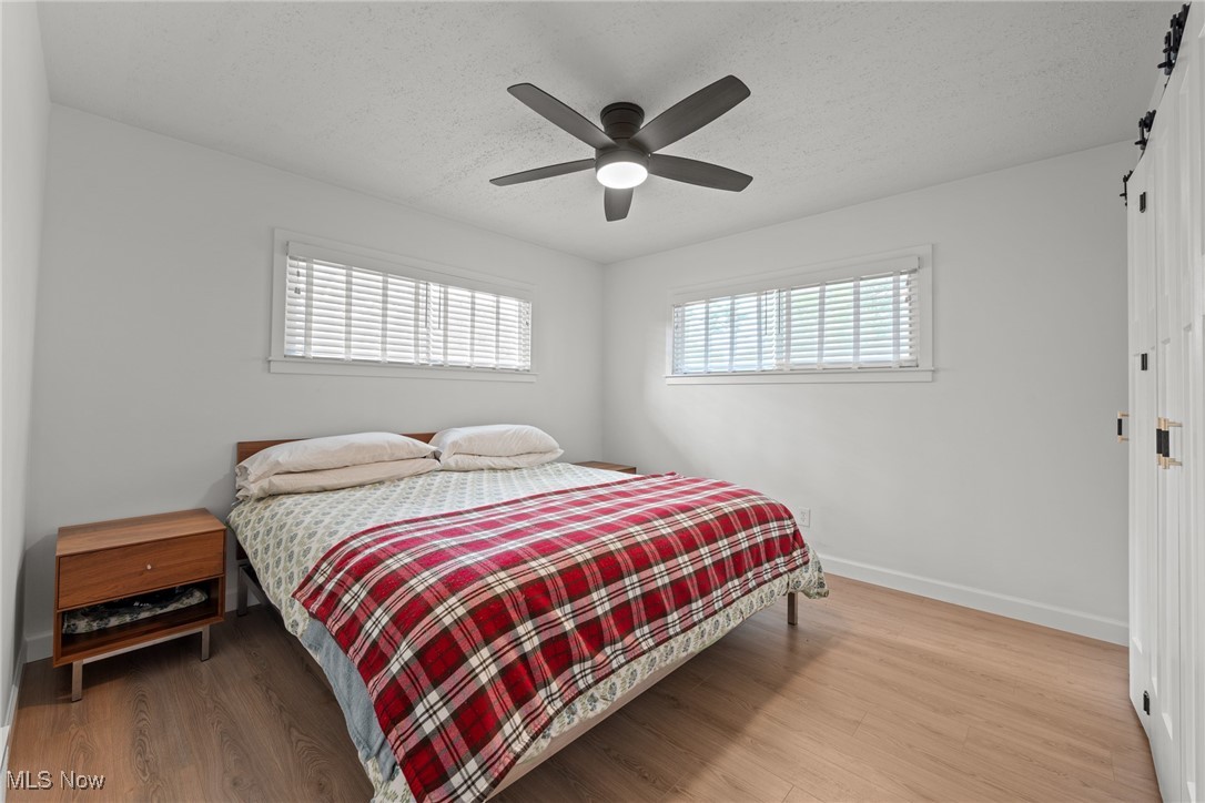 Bedroom with a red plaid blanket, two windows with blinds, and a dark ceiling fan.