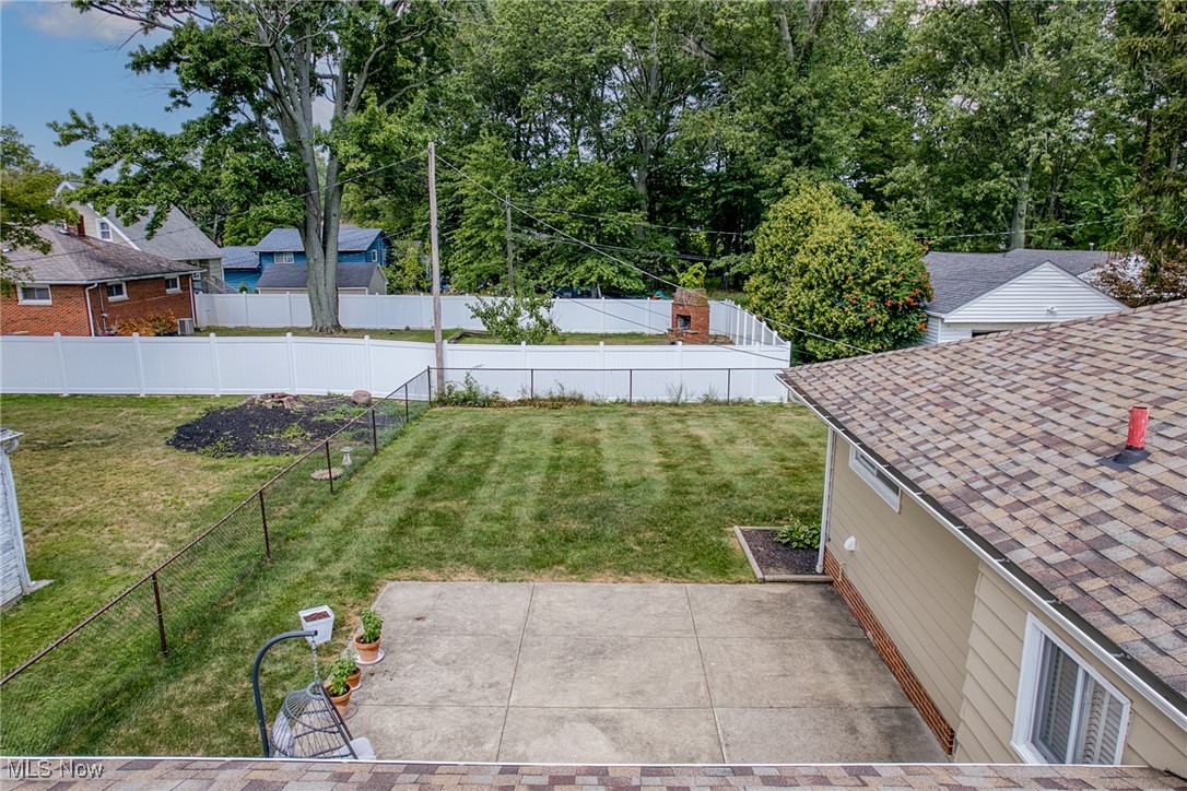 Backyard with a broad lawn, concrete patio, white privacy fence, and leafy trees.