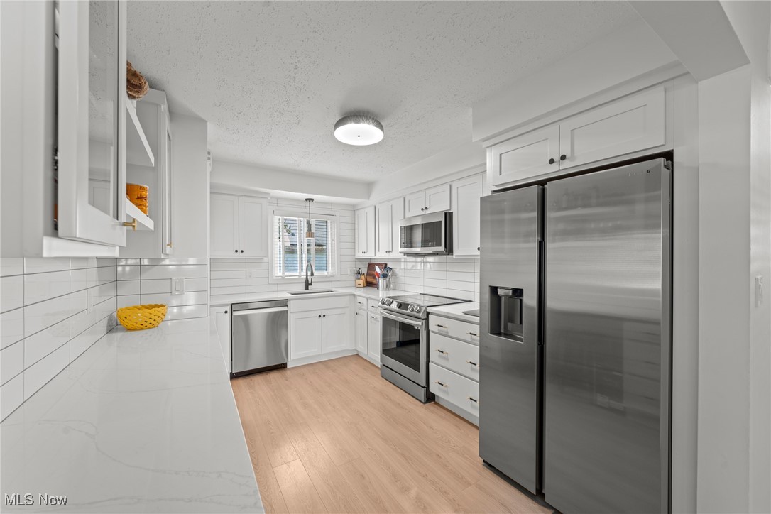 Bright white kitchen with stainless steel appliances, subway tile backsplash, and light wood floors.