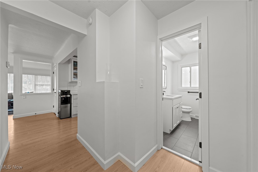 Hallway connecting a kitchen and bathroom, with light wood floors and a white vanity.