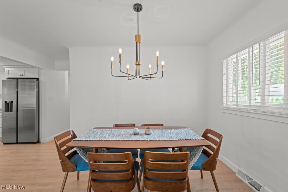 Dining room with a wood table, blue chairs, modern chandelier, and wide shuttered window.