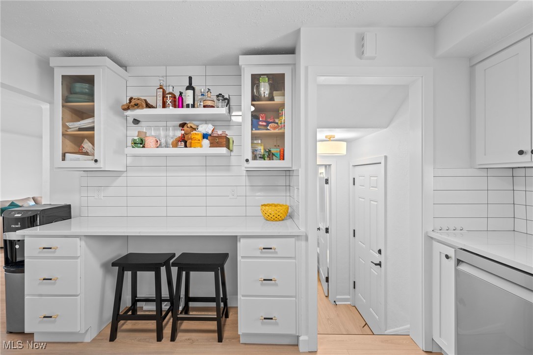 White kitchen with glass-front cabinets, tiled backsplash, and two black stools at the counter.