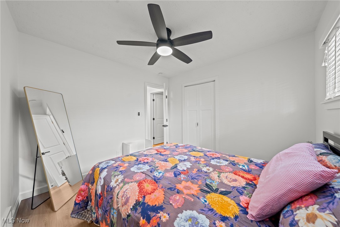 Bedroom with a colorful floral bedspread, pink pillow, black ceiling fan, and leaning full-length mirror.