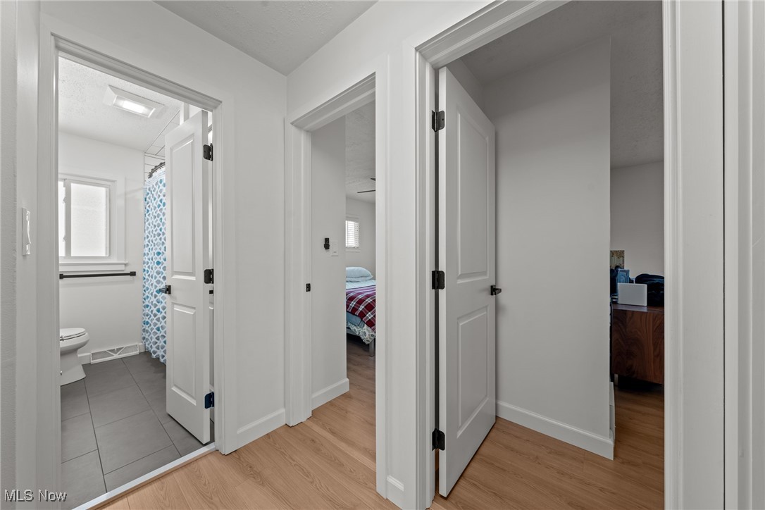 Hallway with light wood floors, open doors, and views into a tiled bathroom and furnished bedrooms.
