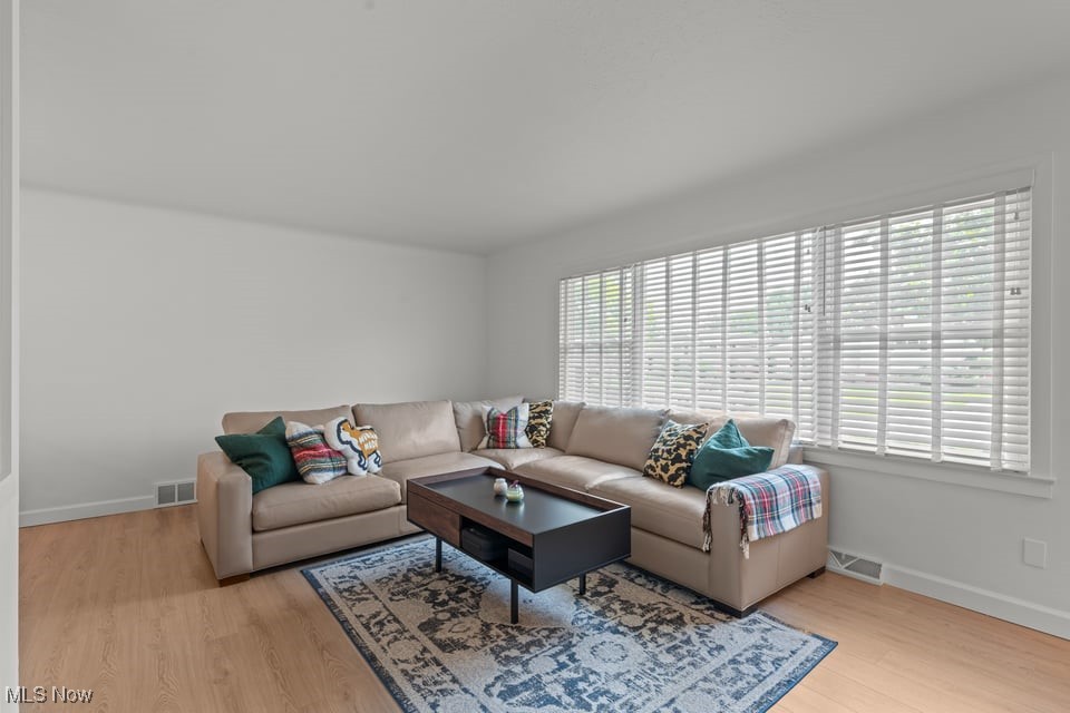 Living room with a beige sectional, patterned rug, dark coffee table, and wide windows with white blinds.