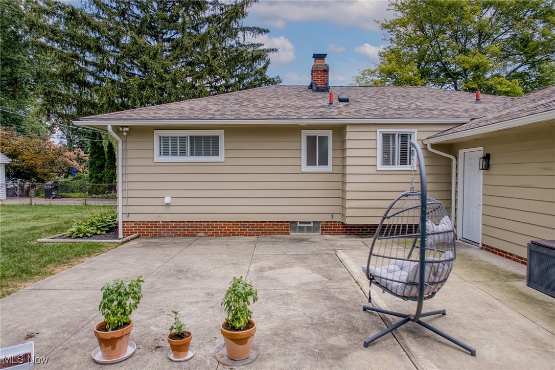 Rear exterior of a beige home with a concrete patio, hanging chair, and potted plants.