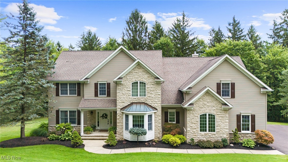 Two-story house with a stone facade, central bay window, and landscaped front lawn.