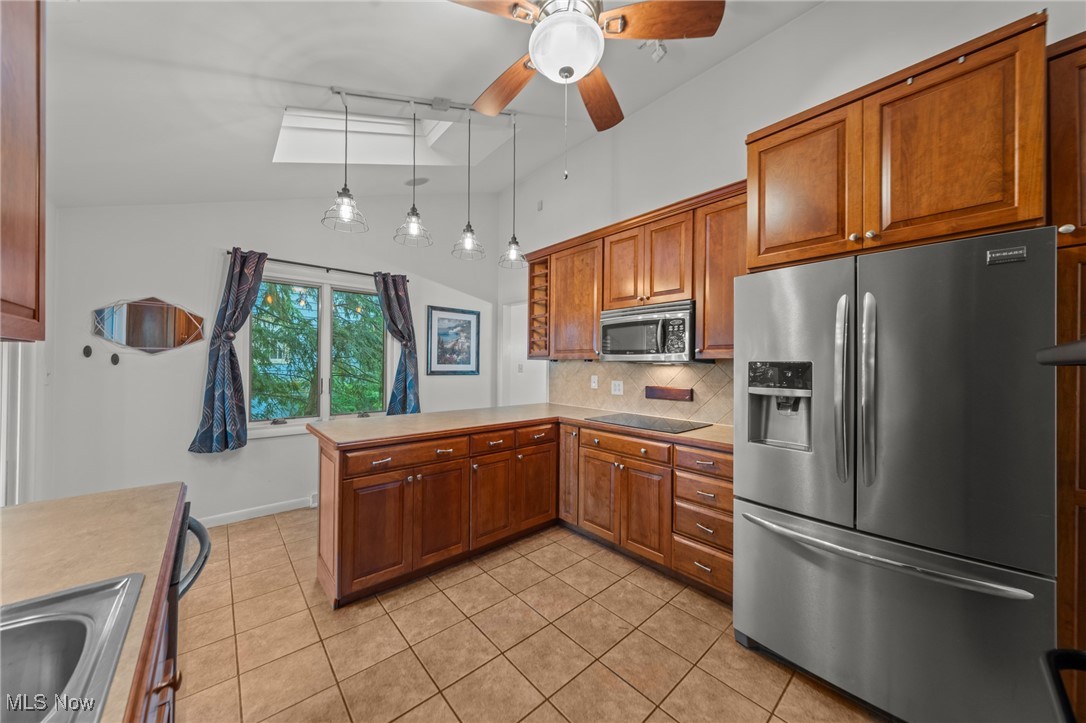 Kitchen with wood cabinets, stainless steel appliances, and a window overlooking trees.