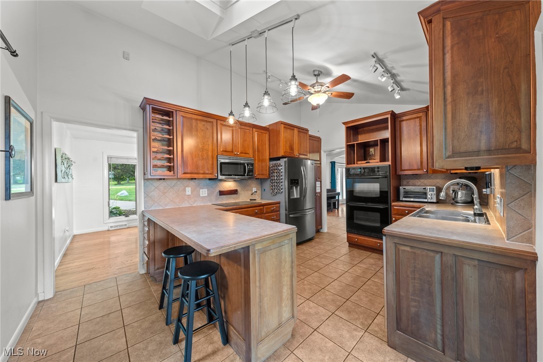 Kitchen with warm wood cabinetry, central island, stainless appliances, and tile flooring.