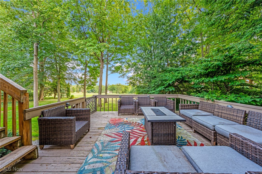 Furnished wooden deck with wicker seating, colorful rug, and leafy trees overlooking a green lawn.