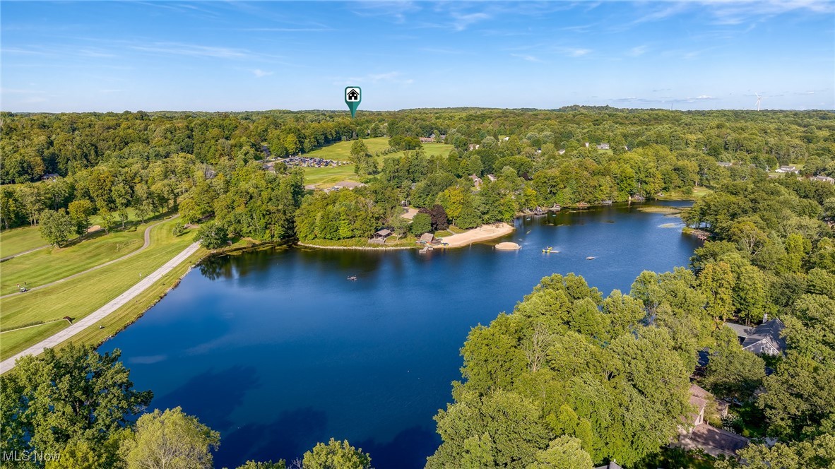Aerial view of a wooded lake with a small sandy beach and homes along the shoreline.