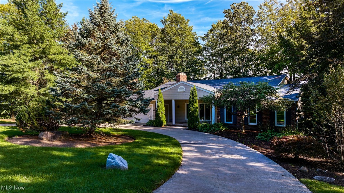 Single-story home with a curved driveway, covered entrance, and mature trees around the lawn.