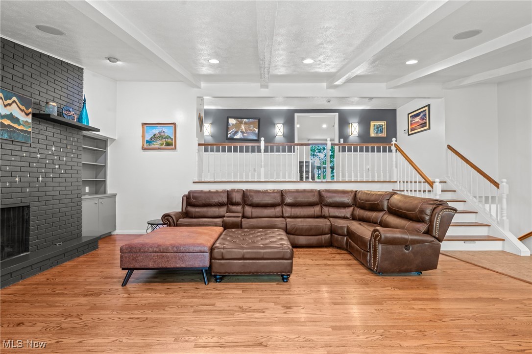 Living room with brown leather sectional, brick fireplace, hardwood floors, and staircase.