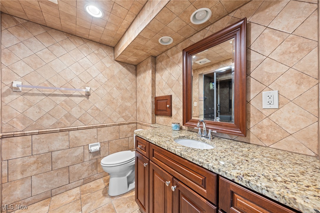 Bathroom with tan tile, a granite-topped wood vanity, and a mirror reflecting a glass shower.